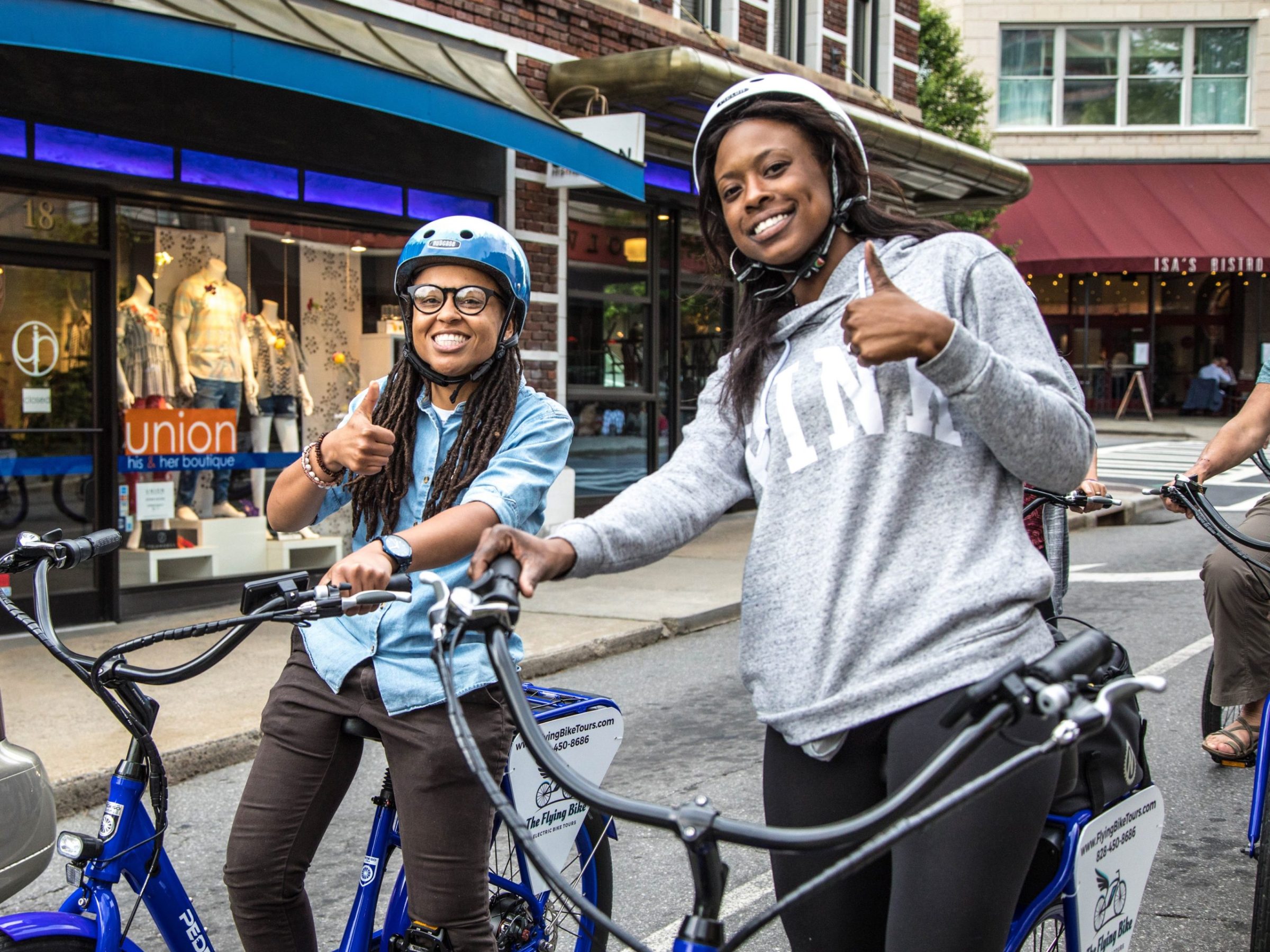 Two people on e-bikes during a custom tour of downtown Asheville and smiling at the camera with two thumbs up