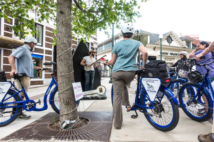 People stopping to listen to a street performer during a group bike tour of Downtown Asheville, NC