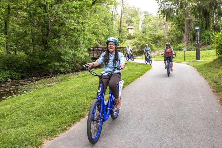 Young woman on a bicycle smiling during a group bike tour along a greenway in Asheville, NC