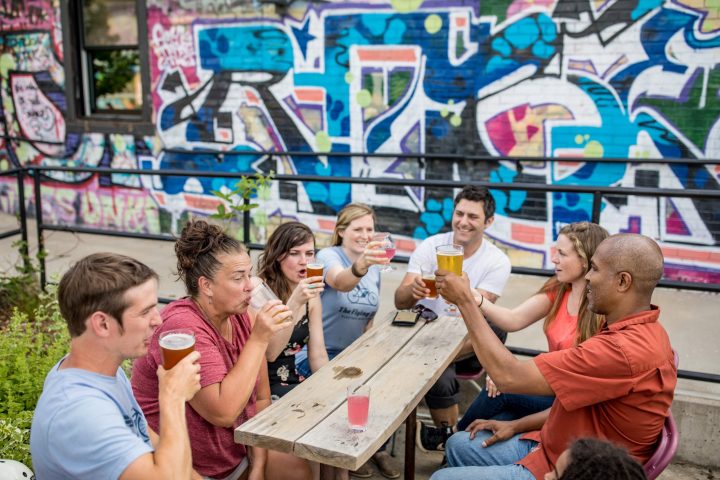 Group of people on an Asheville food tour sitting around a picnic table in front of a graffiti building wall and enjoying beer