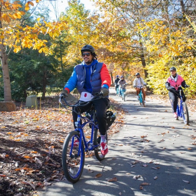 A bike tour guide leads a custom tour on electric bicycles through a colorful park greenway filled with yellow leaves of fall in Asheville, NC