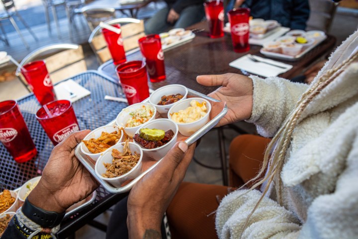 Hands passing a plate with food to another person during a food tour, sitting around and outdoor table.