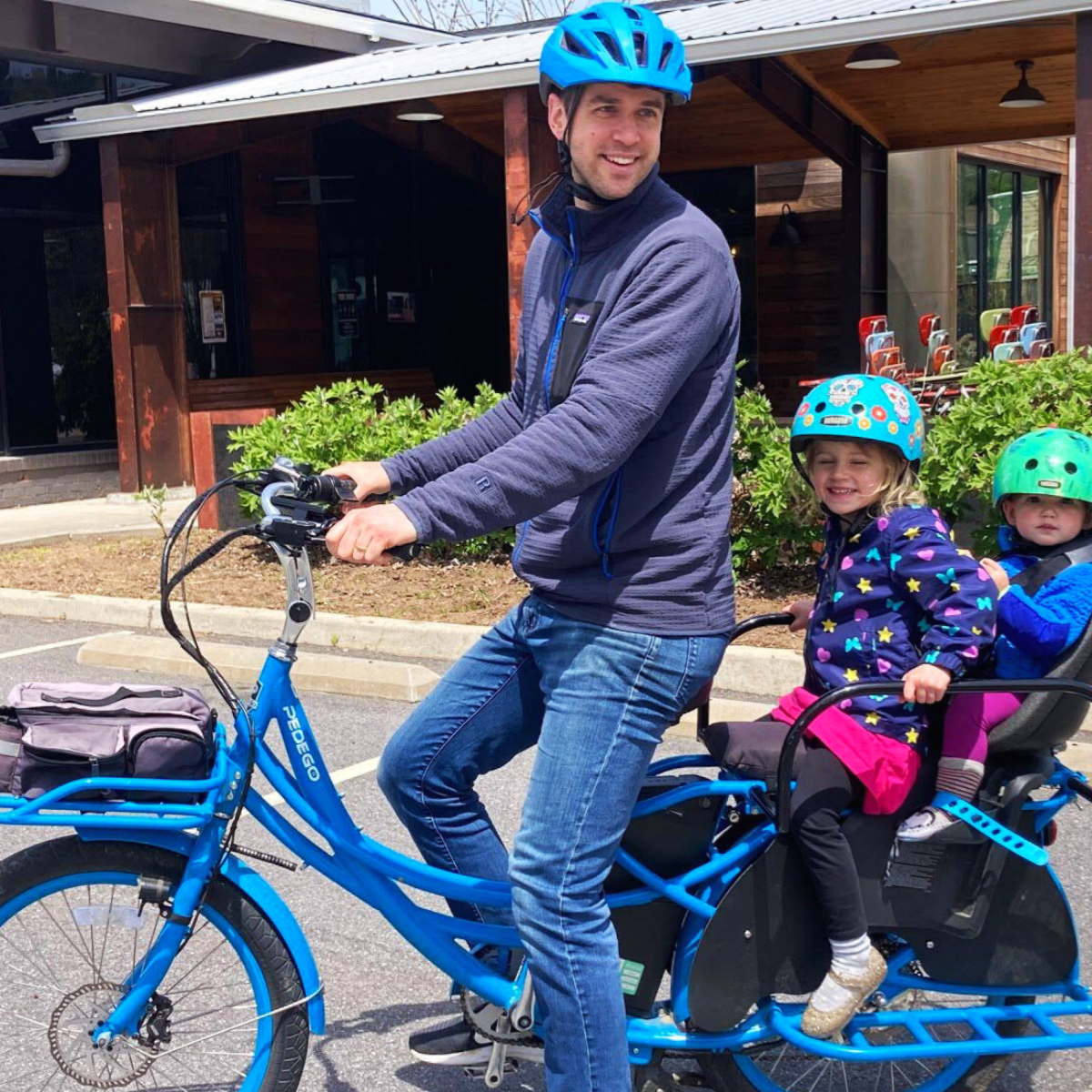 Man on a cargo e-bike with two children riding on the back