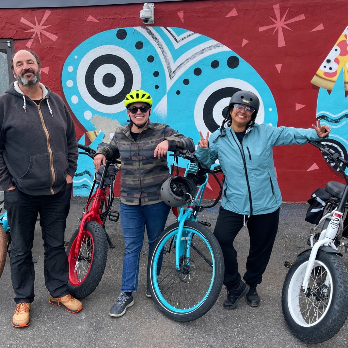 Group of people standing with their bicycles during a bike tour stop and an art-covered wall in Asheville, NC