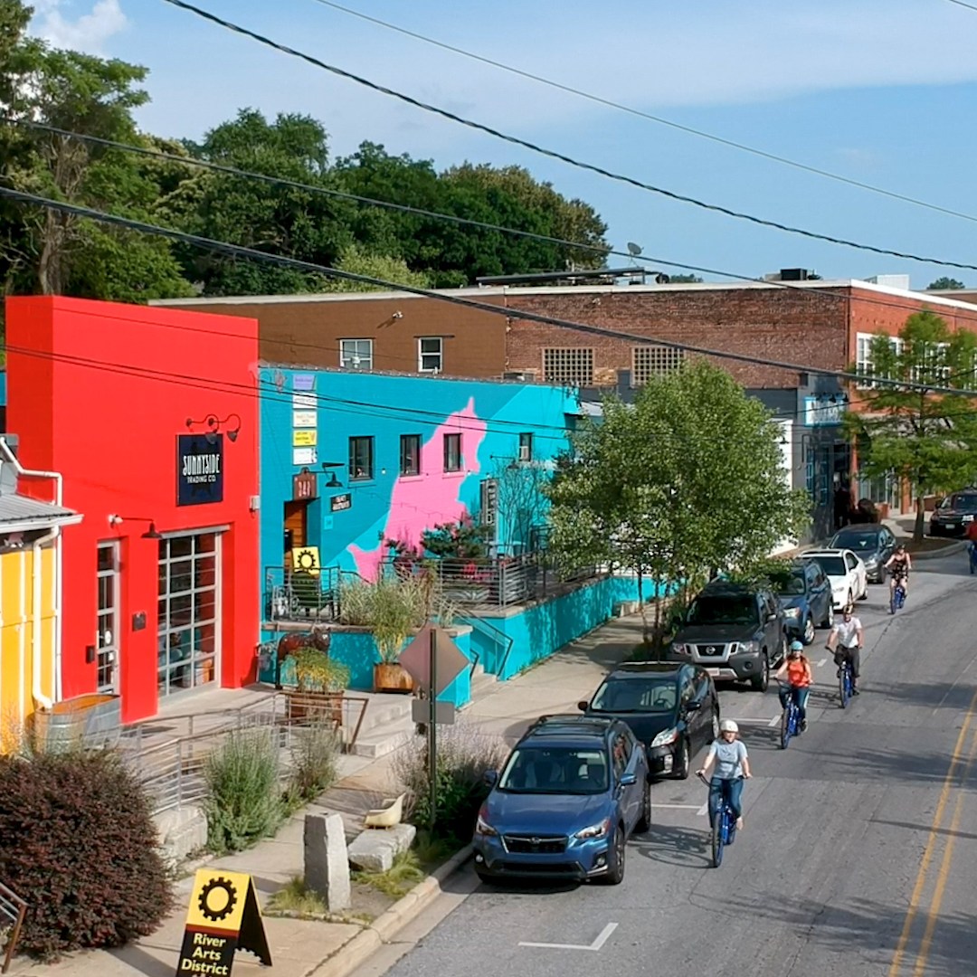 A group of people are riding bikes through the River Arts District streets on an e-bike tour, surrounded by colorful buildings filled with art studios.
