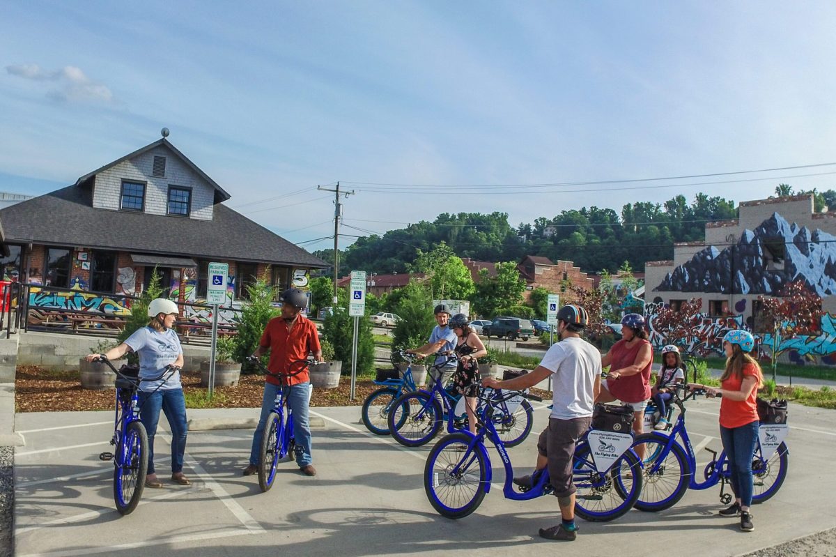 A group gathered in the River Arts District of Asheville on an electric bike tour surrounded by buildings covered in graffiti artwork.