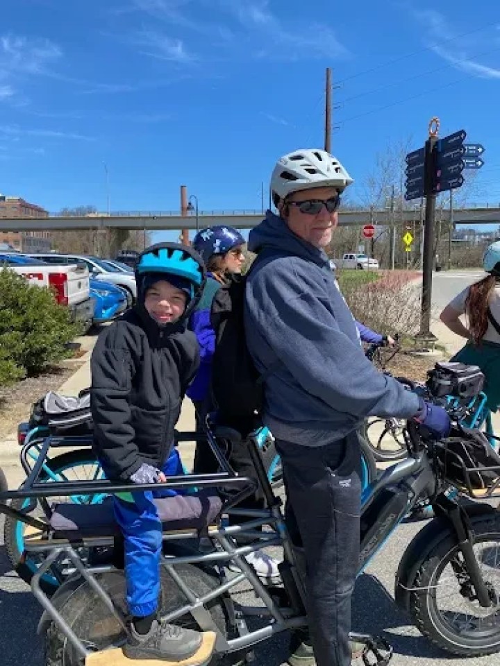 Man and child on a bicycle in a parking lot under a blue sky.